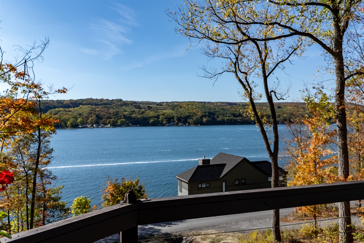 View from deck edge down to lake — glimpse of water, trees, and horizon.