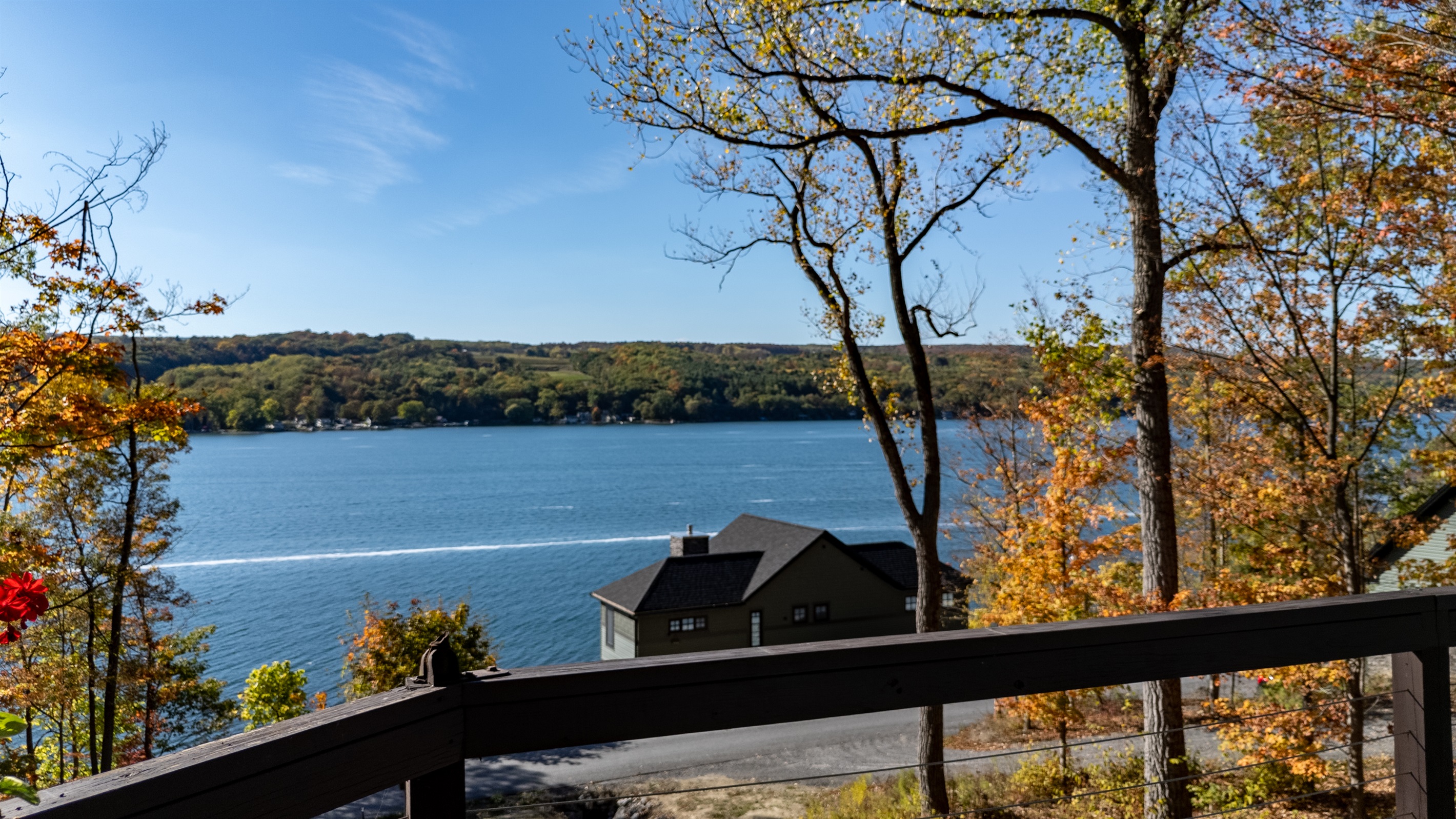 View from deck edge down to lake — glimpse of water, trees, and horizon.