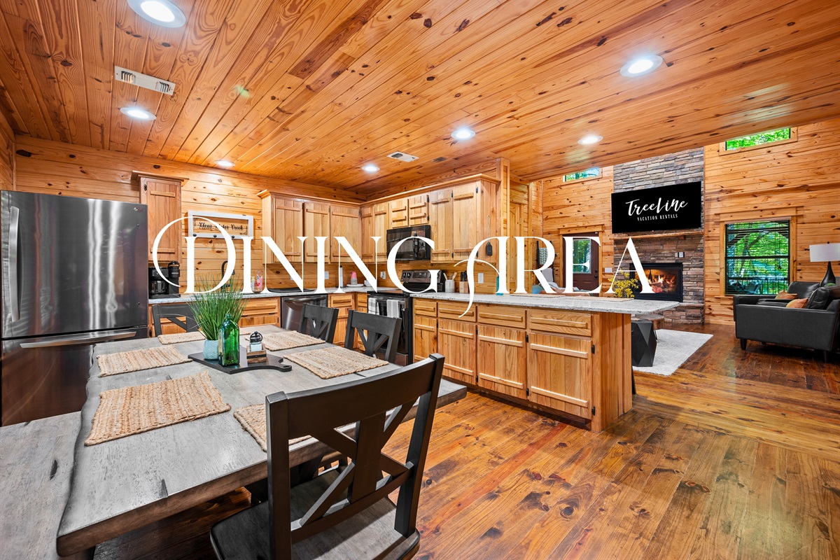 Spacious dining area with farmhouse-style table, surrounded by natural wood walls and adjacent to the kitchen.