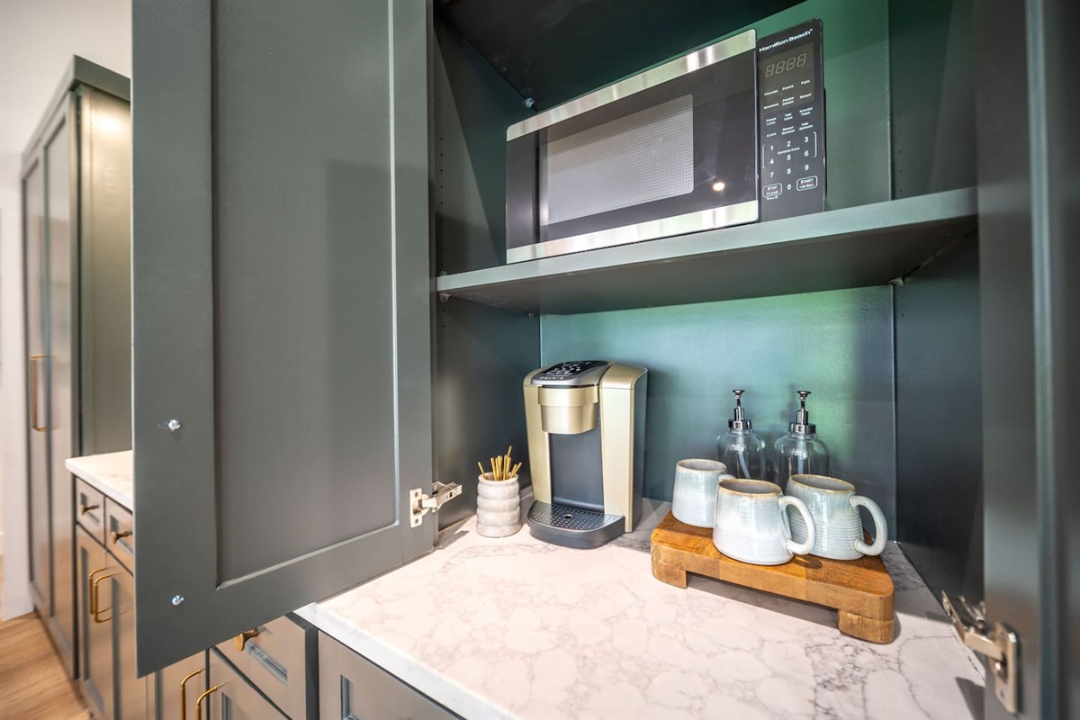 Built-in coffee station with microwave and single-serve coffee maker, stocked with coffee, flavored syrups, creamer, sweeteners, and coffee bar essentials for an easy, elevated morning routine.