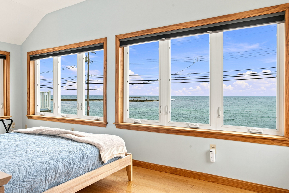 Bright bedroom with expansive windows showcasing stunning coastal scenery.