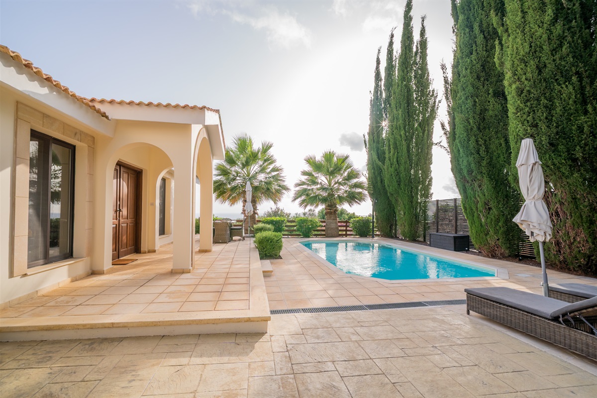 Mature palm trees and cypresses frame the villa and pool, providing natural shade, privacy, and a tranquil setting for relaxation.