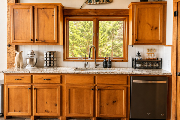 Fully equipped kitchen with warm wood cabinetry, granite countertops, stainless steel appliances, and peaceful wooded views from the kitchen window.