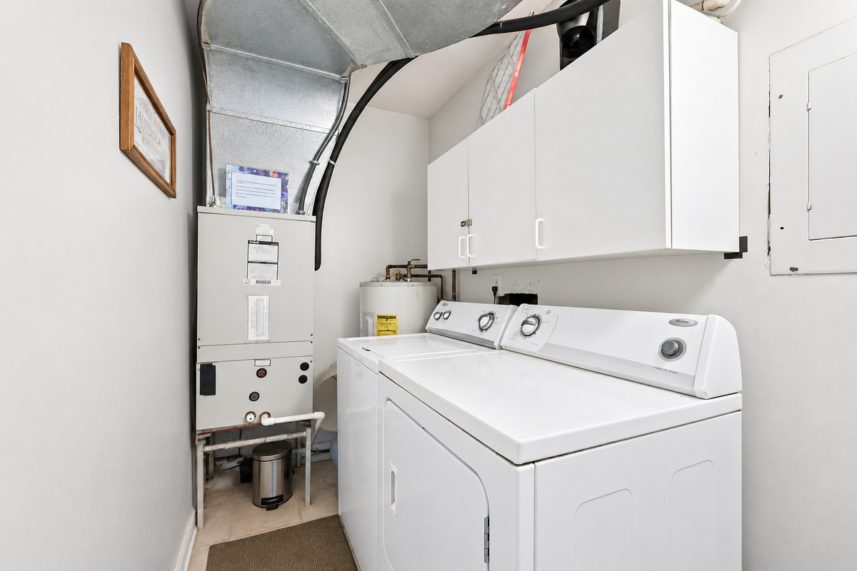 In-unit laundry room with washer, dryer, overhead cabinets, and HVAC equipment tucked away from the main living areas.
