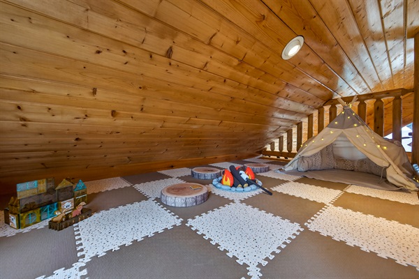 The kids' secret loft hideaway — tucked above the upper bedroom with a teepee, fairy lights, pretend s'mores campfire, wood slice seats, and cabin-themed building tiles. They'll disappear up here for hours.