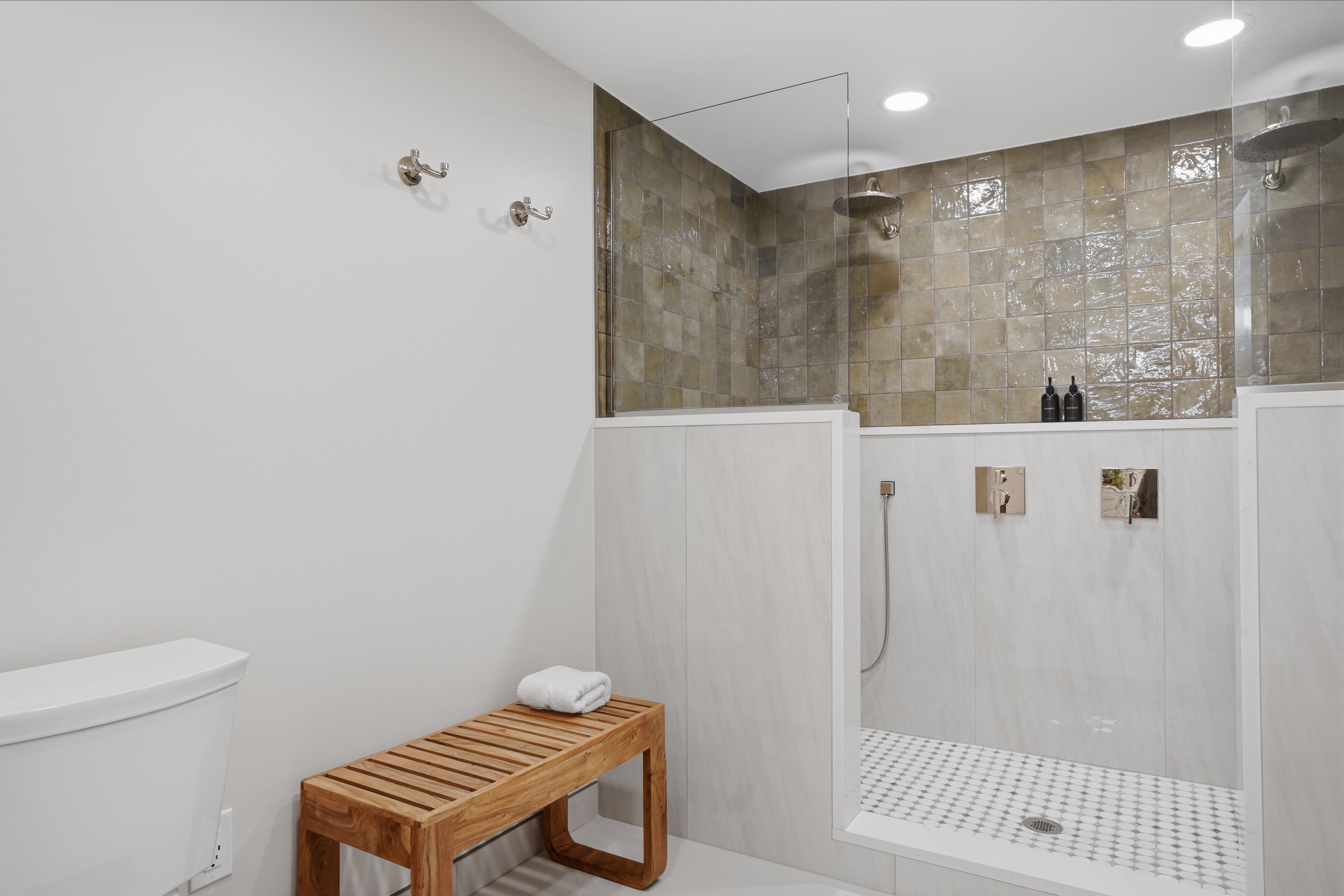 Spa-style walk-in shower with stone tile walls, glass partition, and built-in bench. Clean, modern design with warm tones and a calm, upscale, hotel-like feel.