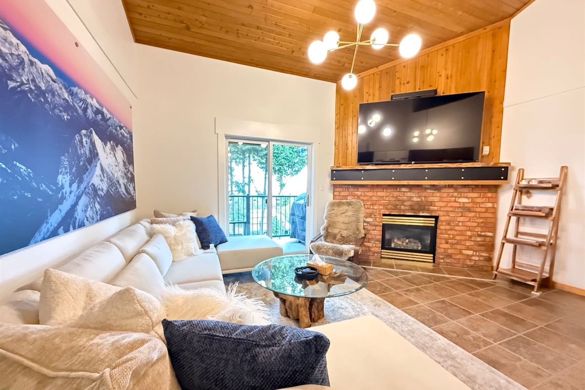 Main Living Area: An open-concept living room featuring vaulted cedar ceilings, a gas fireplace, and a large 78-inch Smart TV surrounded by alpine-inspired décor.