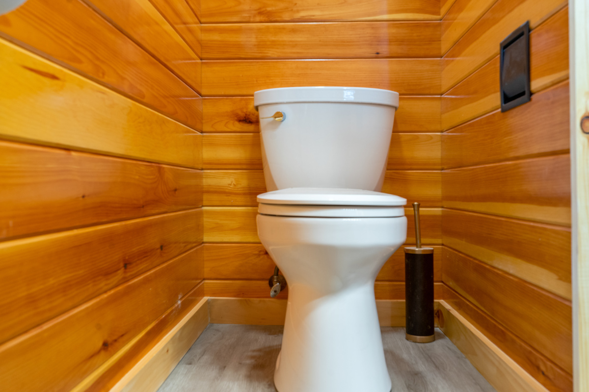 Appreciate the meticulous cleanliness of the private toilet alcove. Surrounded by warm, polished wood paneling and featuring durable gray flooring, this neatly tucked away space ensures privacy and complete sanitation for a comfortable stay.