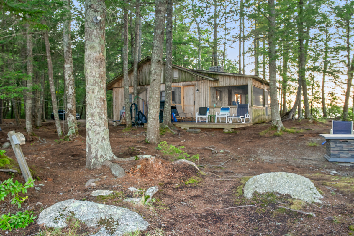 East side view of Loonrise Point from the dock path! Features an open kitchen deck with seating and gas grill, screened porch, and lakeside fire table on the right. Natural pine floor with granite rocks on Beech Hill Pond in Otis, ME, near Acadia.
