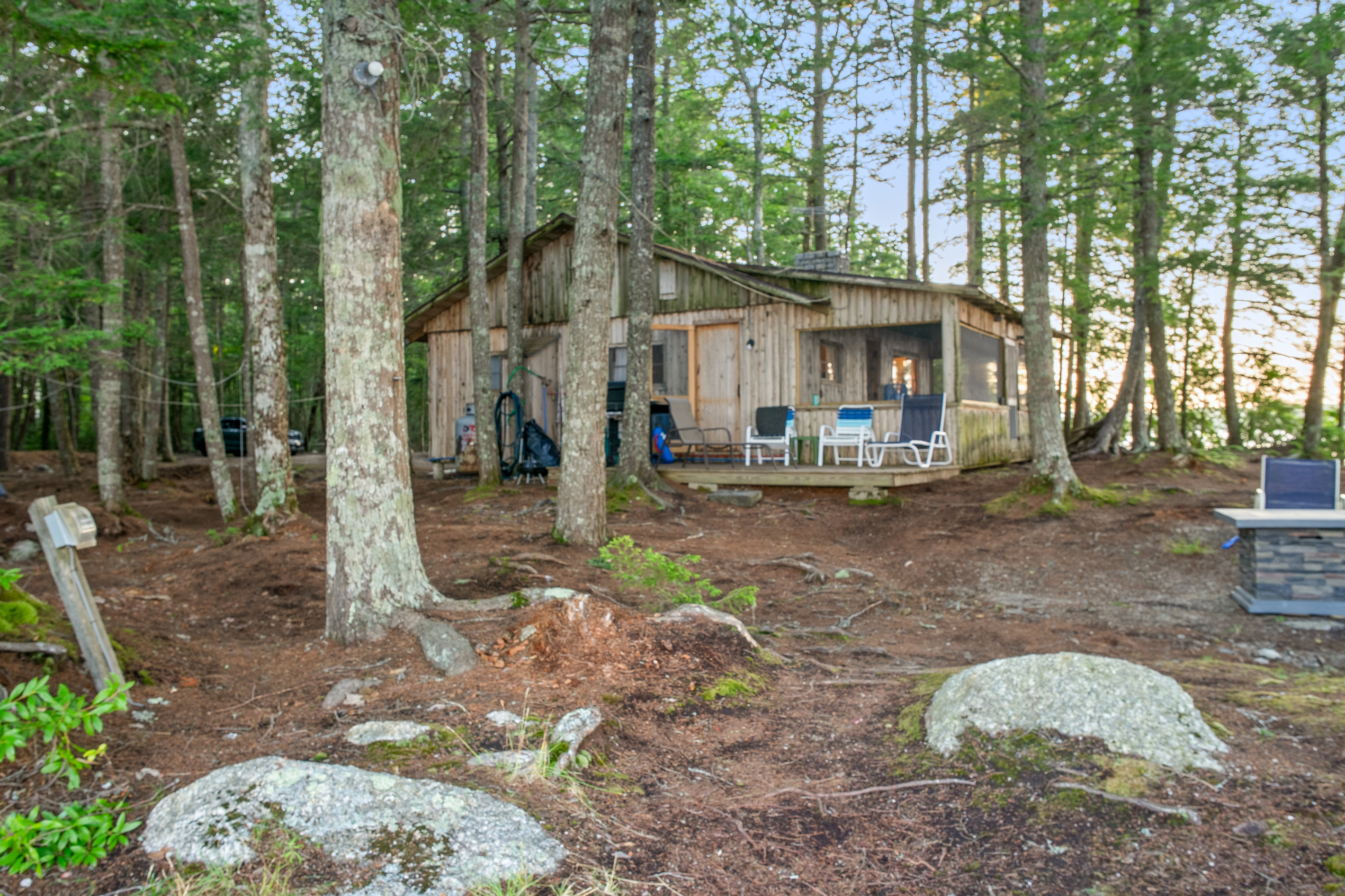 East side view of Loonrise Point from the dock path! Features an open kitchen deck with seating and gas grill, screened porch, and lakeside fire table on the right. Natural pine floor with granite rocks on Beech Hill Pond in Otis, ME, near Acadia.