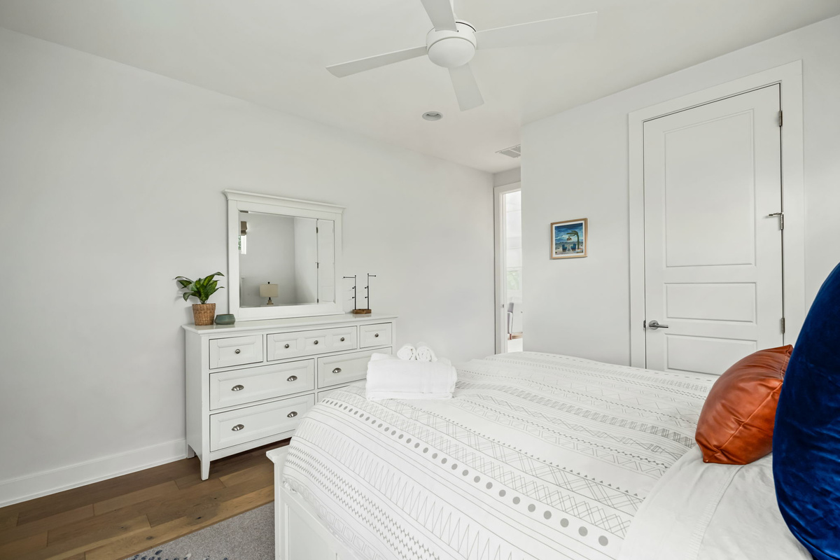 Bright bedroom featuring a queen bed with colorful accent pillows, a spacious dresser, and easy closet access.