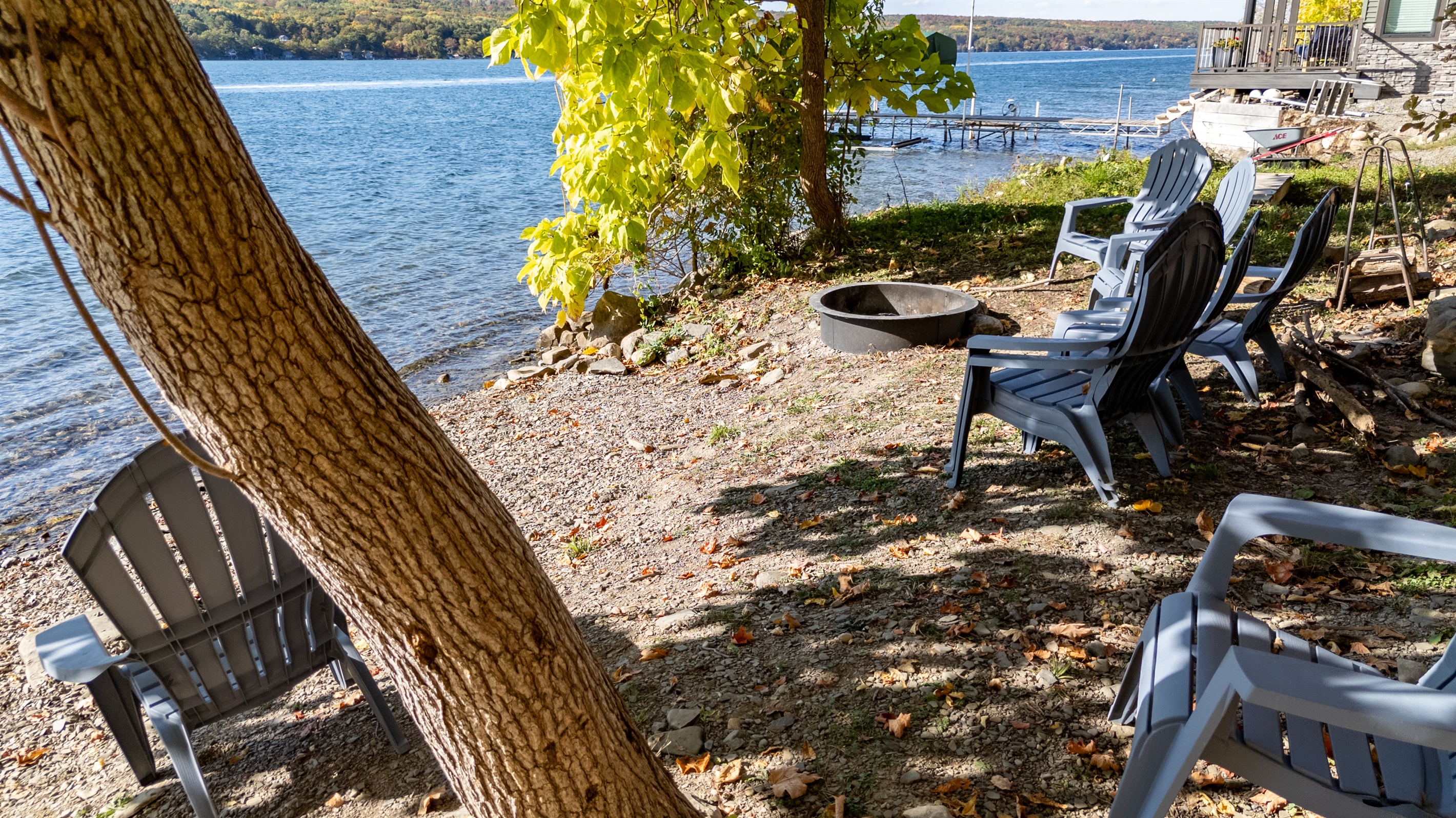 Closer view of lakeside fire-pit and seating positioned between trees.