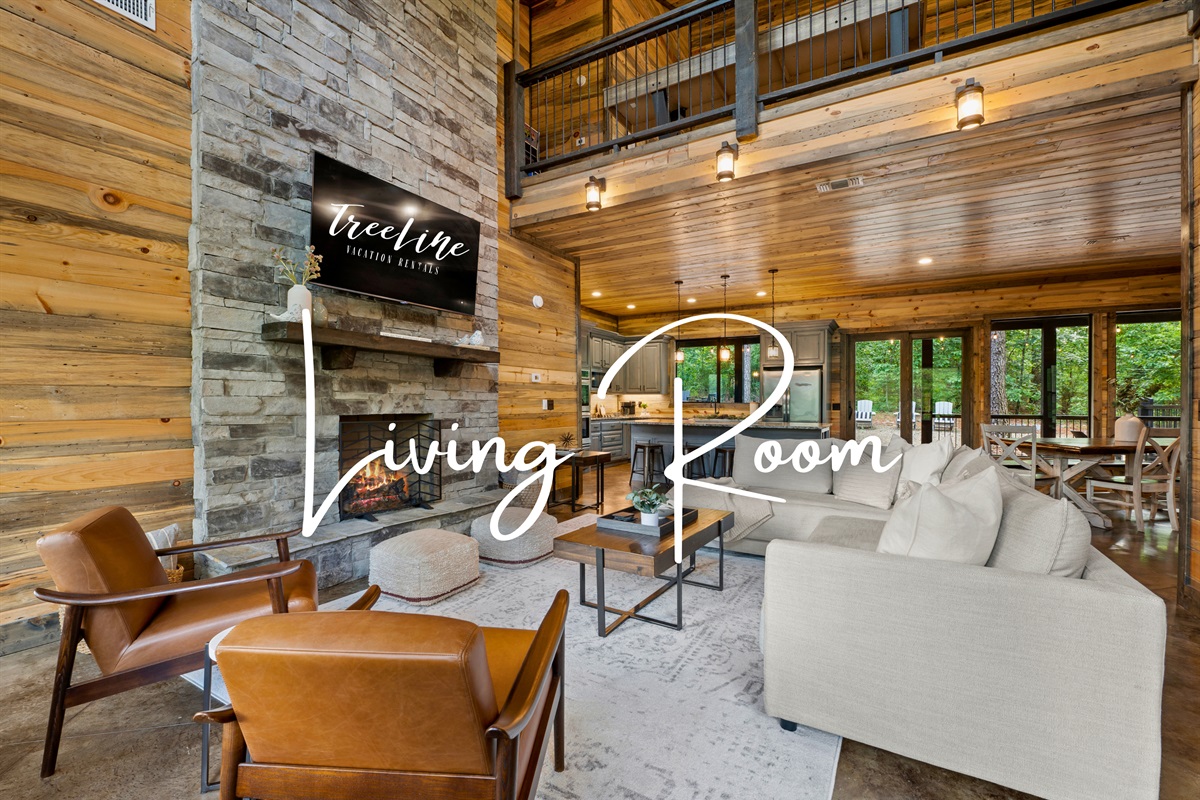 Relax in the spacious living room featuring contemporary furnishings, a stone fireplace, and a tall, wood-paneled ceiling that opens up to the dining area