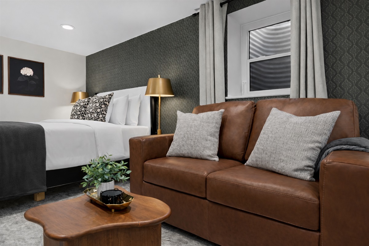 Warm, modern studio space with a plush bed, cozy leather seating, soft lighting, and stylish details—perfect for relaxing and feeling right at home.