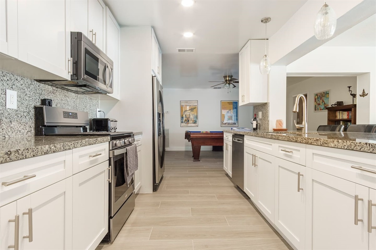 View from the kitchen toward Pool table and Game room.  Kitchen cupboards are stocked with cookware,dishware, glassware, table settings for the dining room, as well as plastic-ware for poolsidedining.