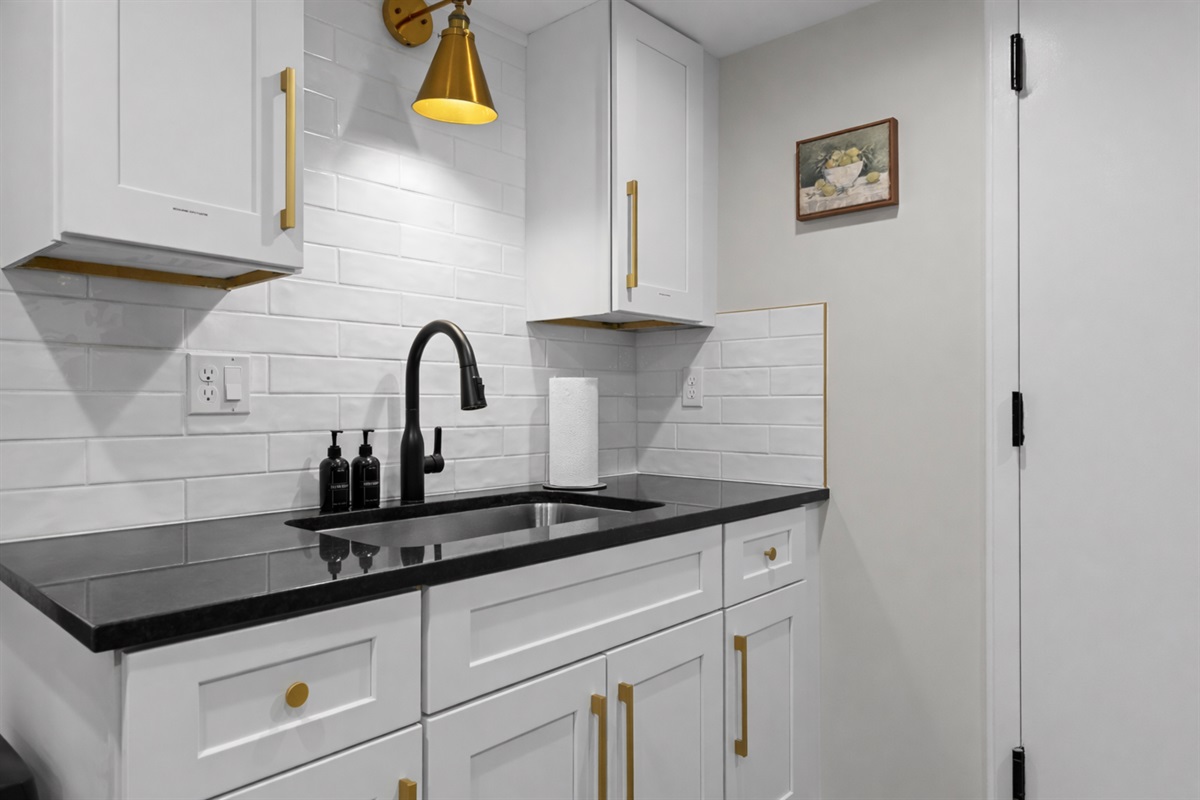 Clean, modern kitchenette with sleek black counters, subway tile backsplash, stylish fixtures, and smart storage for a comfortable stay.