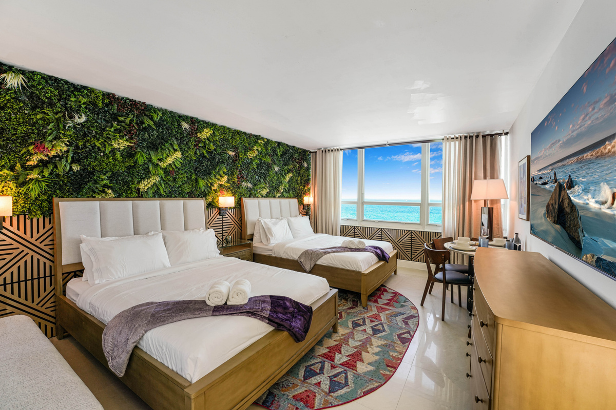 Two premium queen beds with memory foam hybrid mattresses and crisp white linens, set against the greenery and wood feature wall.
