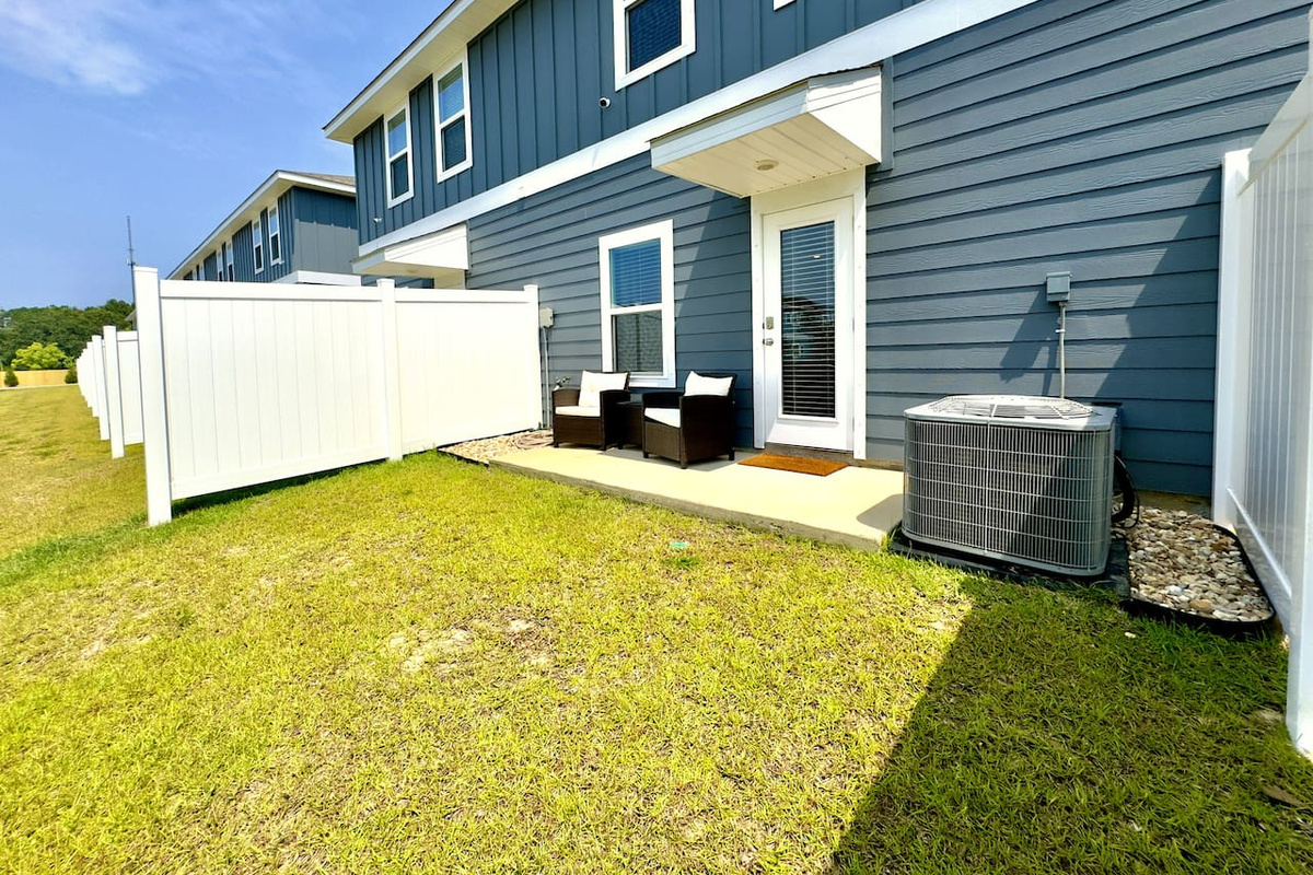 Stepping outside, soft grass underfoot, warm sun overhead. The private patio invites a cold beer, good conversation, or a grill session with friends. Coastal blue siding, fresh air, easy and open.