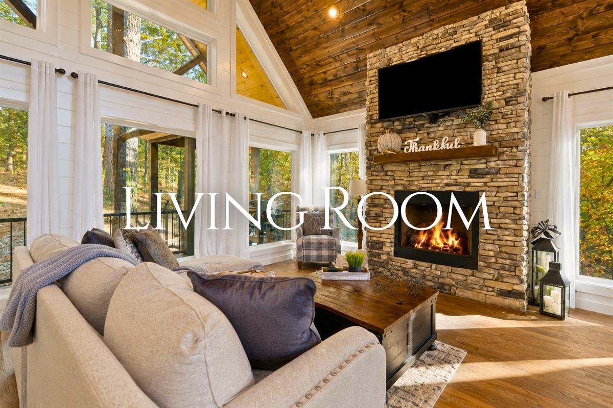 The cozy living room features soaring ceilings, oversized windows, and a beautiful stone fireplace that creates the perfect spot to relax after a day of adventure.