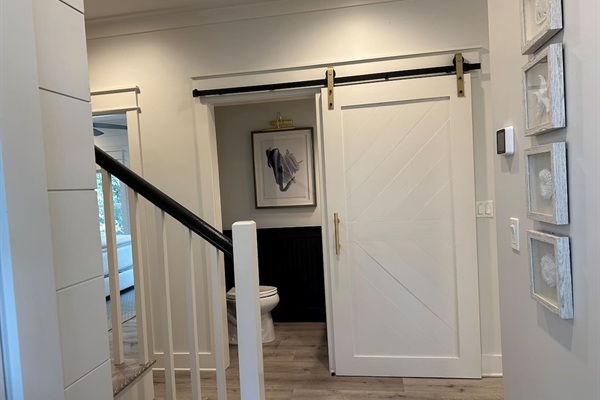 A stylish half bath off the entryway, conveniently located between the first-floor king suite and kitchen. Features a modern barn door, coastal accents, and easy access for guests.