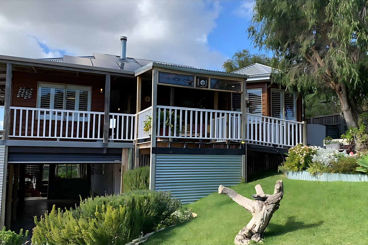 Lake Views & Coastal Escape is a raised timber home with white-railed verandas, solar panels and parking underneath, set above a landscaped lawn on a quiet Preston Beach street.