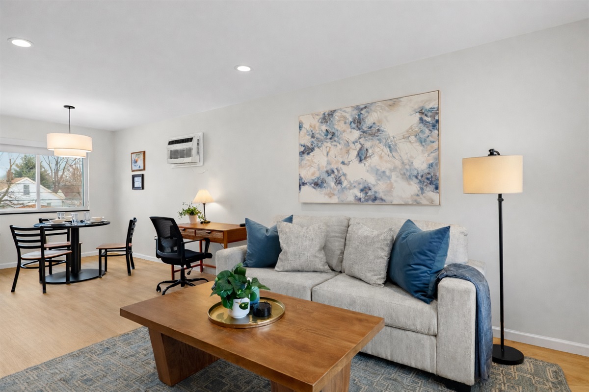 Open, sun-filled living space with cozy seating, dedicated workspace, and dining area—perfect for relaxing, working, and enjoying meals at home.