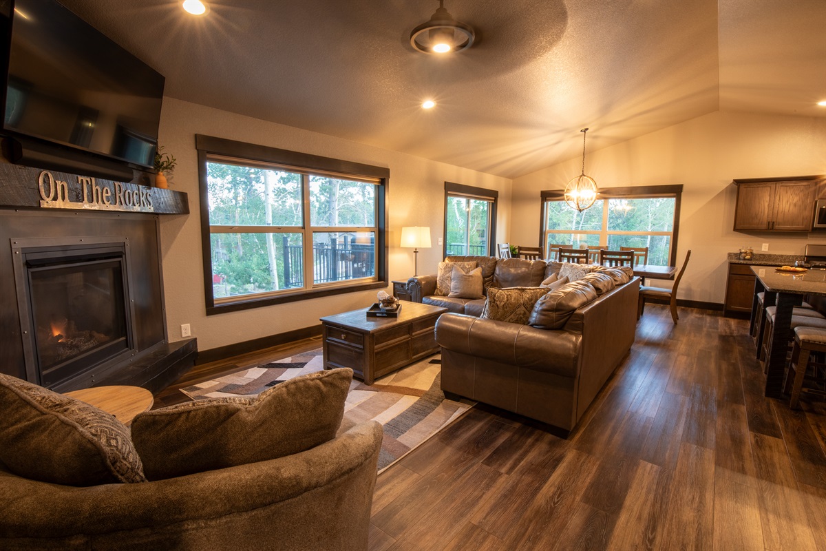Visualize lounging in the expansive living space at "On The Rocks," where the cozy fireplace flickers warmly beside a large TV. 