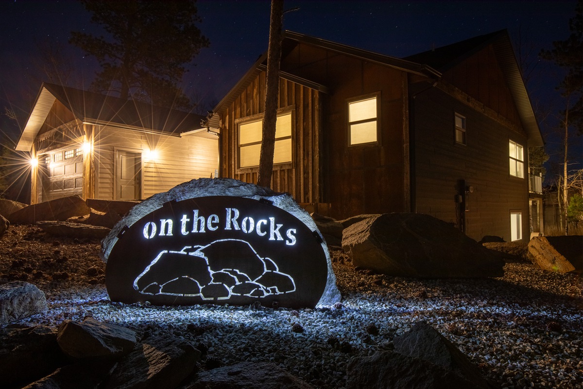 A warm glow lights up the cabin as the custom On The Rocks sign shines against the dark sky—an inviting welcome when you arrive after a day of Black Hills adventures.