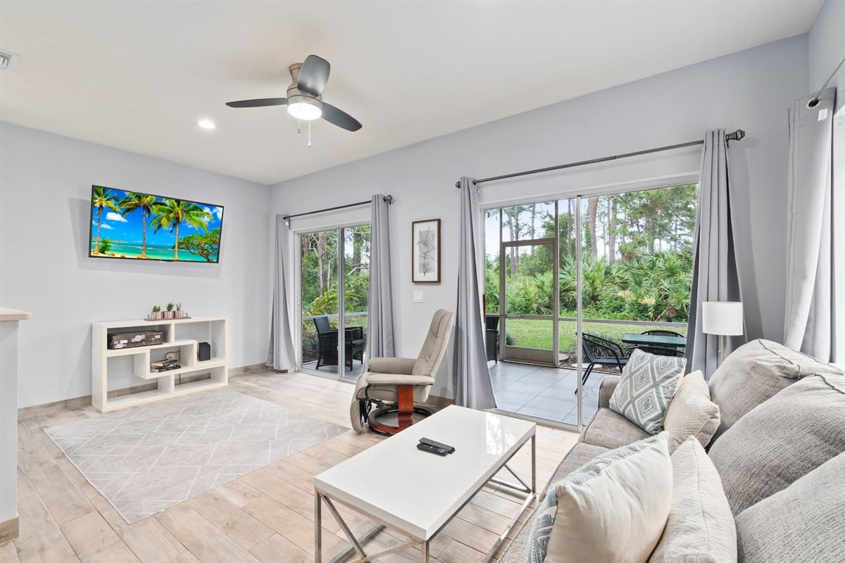 Comfortable living area with modern furnishings, large TV, ceiling fan, and sliding glass doors leading to the screened patio.