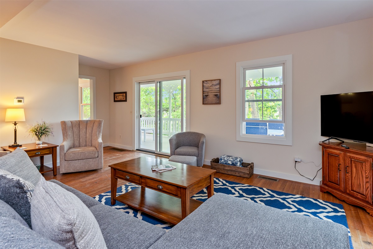 Relax in a bright living room with a large sliding door opening to the porch, surrounded by lush greenery and peaceful lake views.