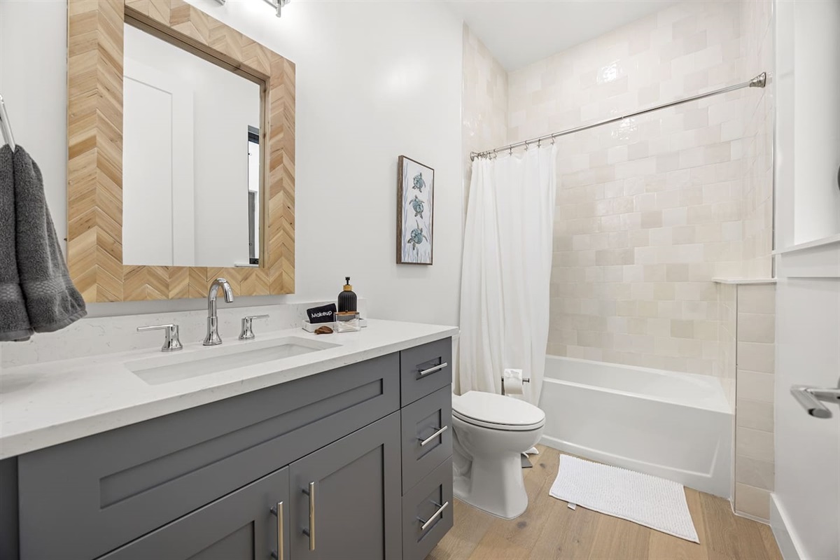 Relax in this elegant bathroom featuring a sleek toilet, a stylish sink with a modern faucet and a functional drawer below, a beautiful design mirror on the wall alongside a beautiful bathtub for ultimate comfort and relaxation.