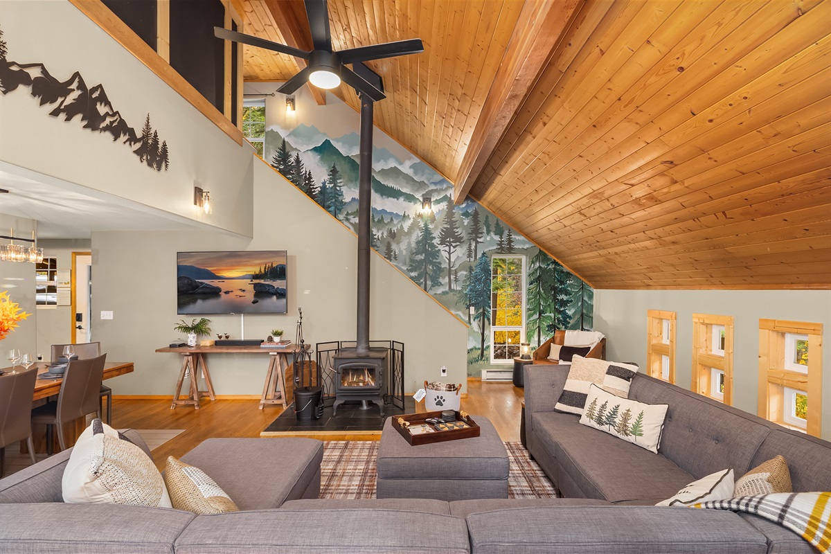 Open living room and dining room with wood burning stove, stunning mural and French doors out to the upper deck