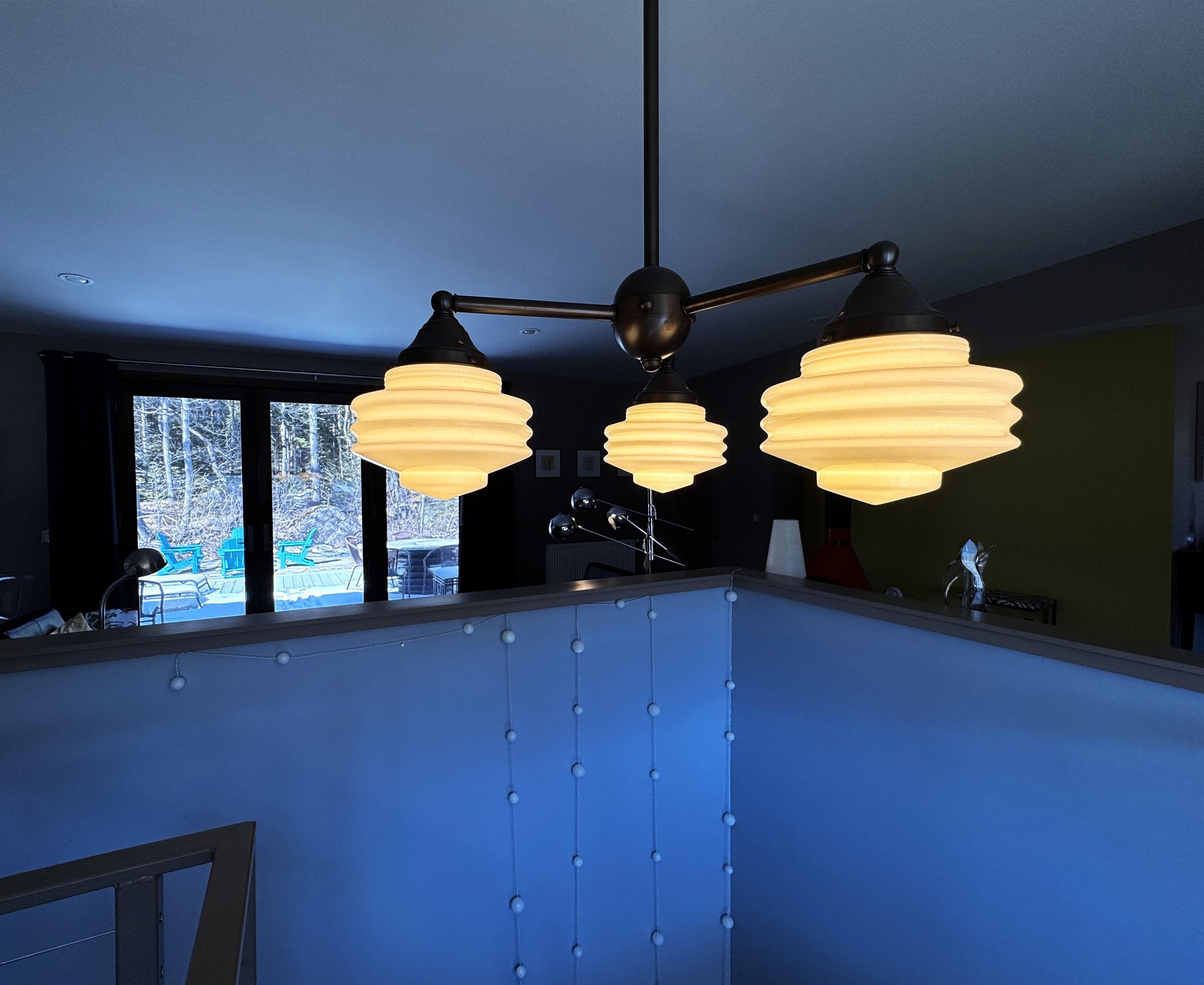 Modern designer lighting over the main stairway, framed by large picture windows and a direct-access door to the 33ft "Park Border" deck. This bright transition offers a seamless indoor-outdoor flow at the edge of Acadia National Park.