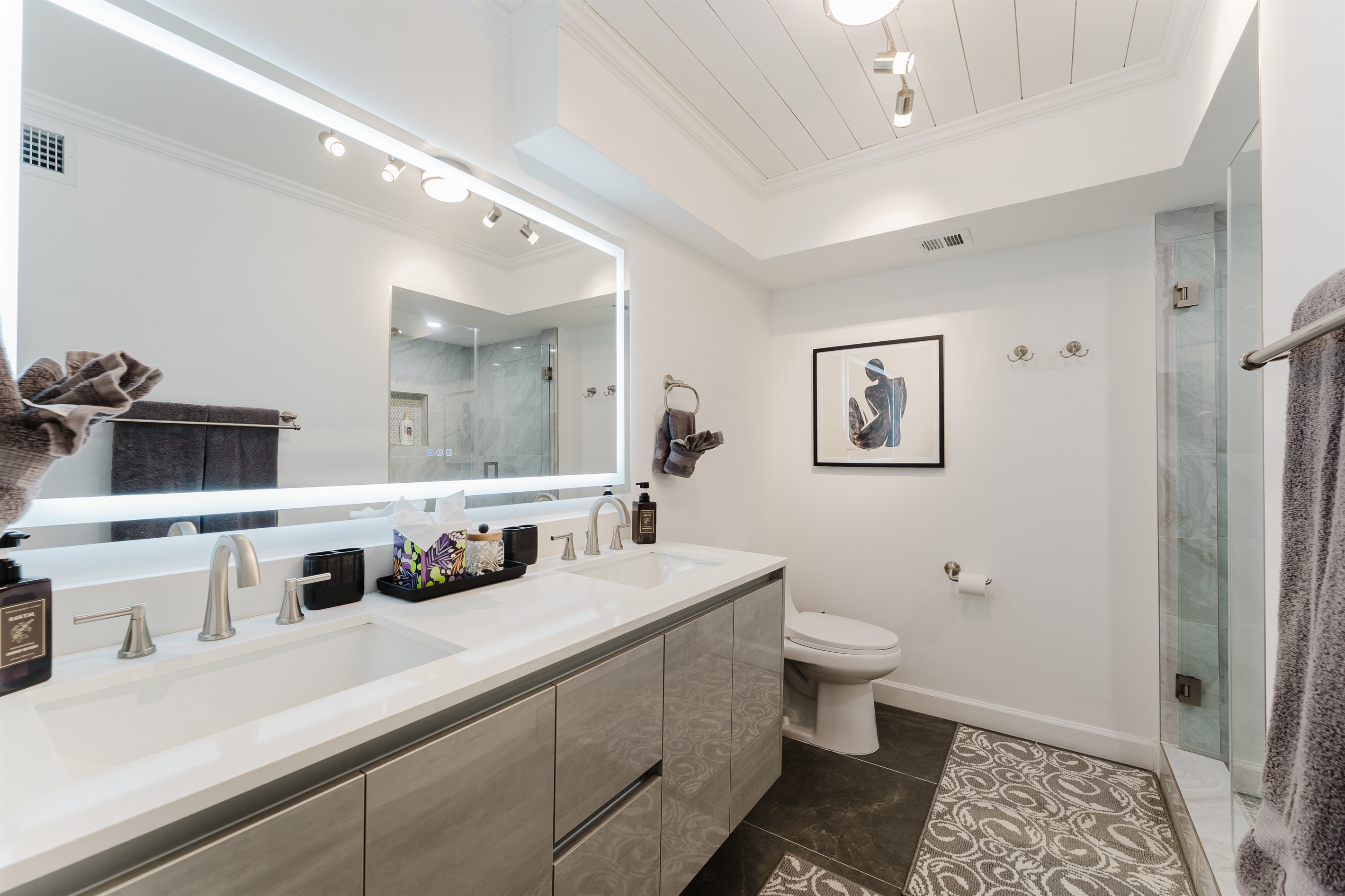 Spacious primary bathroom with double vanity, LED-lit mirror, and modern walk-in glass shower