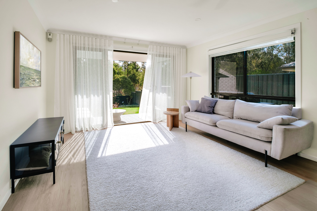 The living room has a generous sofa, bright windows and direct access to the patio and garden outlook.
