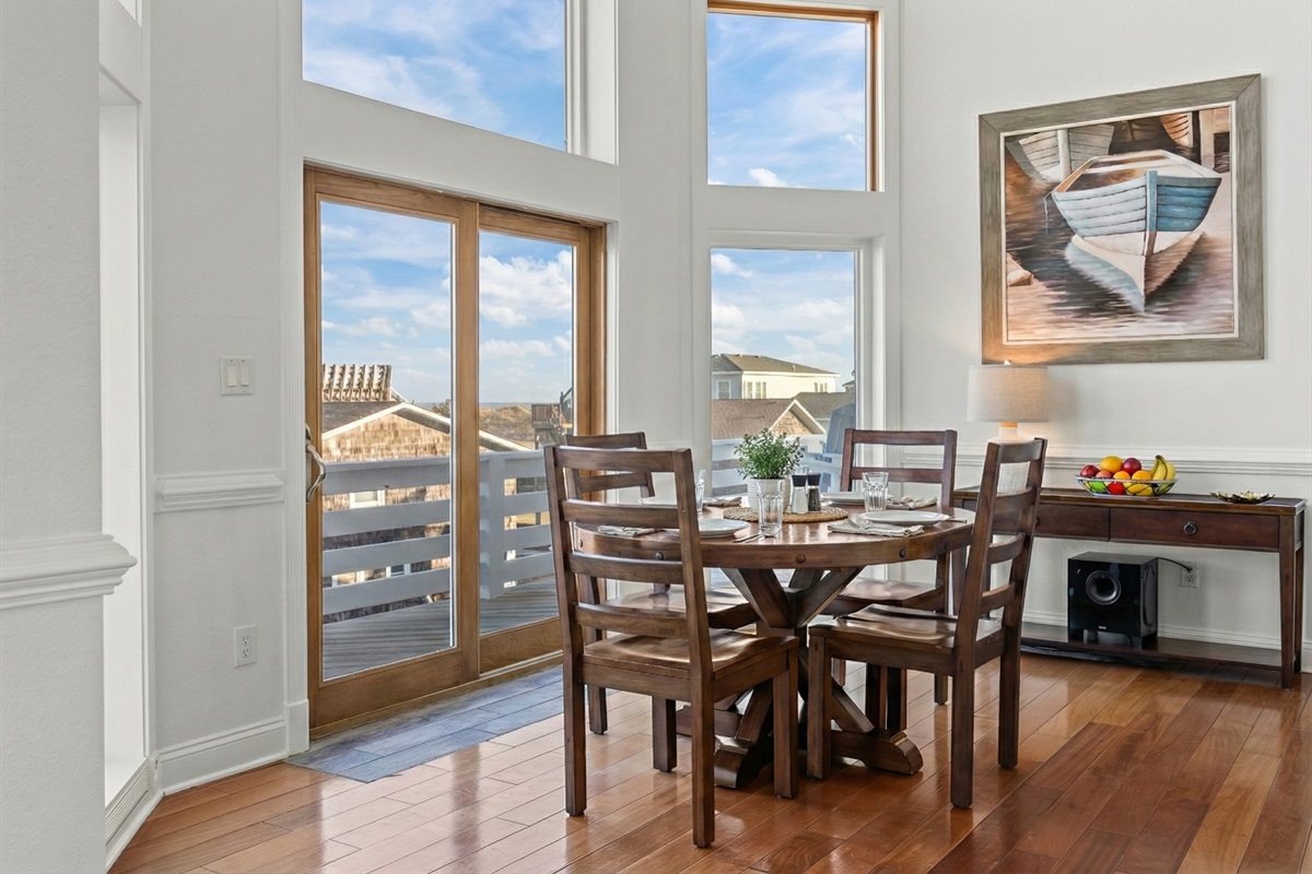 Bright dining area with a large table for gathering, featuring sliding glass doors that frame the ocean view.