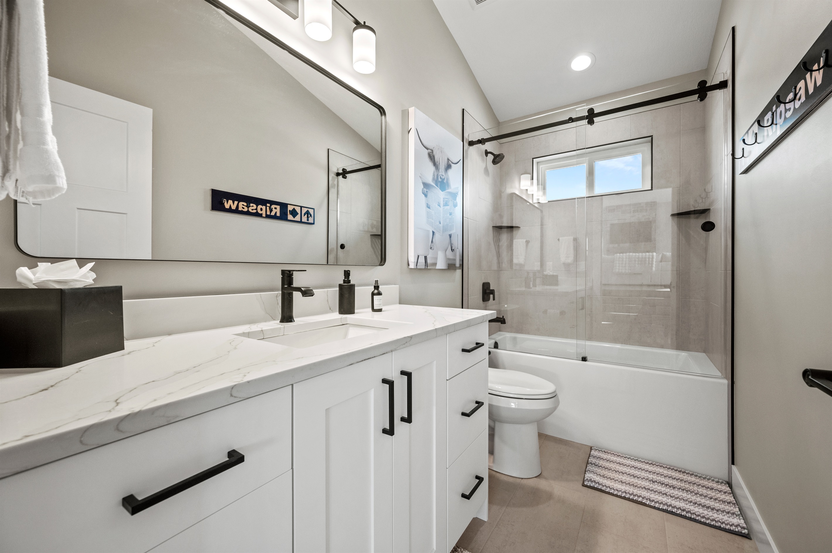 Spacious bathroom with quartz countertops, large mirror, and a tub-shower combo with sleek glass doors.
