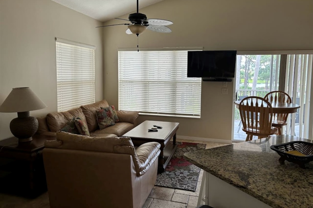 Comfortable living area with cozy seating, wall-mounted TV, ceiling fan, and natural light from the balcony doors.