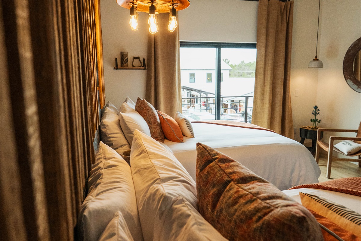 The Corral Suite bedroom — two queen beds, a bright window, and premium Comphy linens in a modern Western setting.