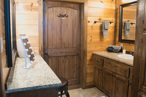 Private bathroom inside primary bedroom with a tub/shower combo, warm wood finishes, stone-look tile surround, 2 vanity areas, and plenty of cabin character. Hollywood lighted mirror available under counter.