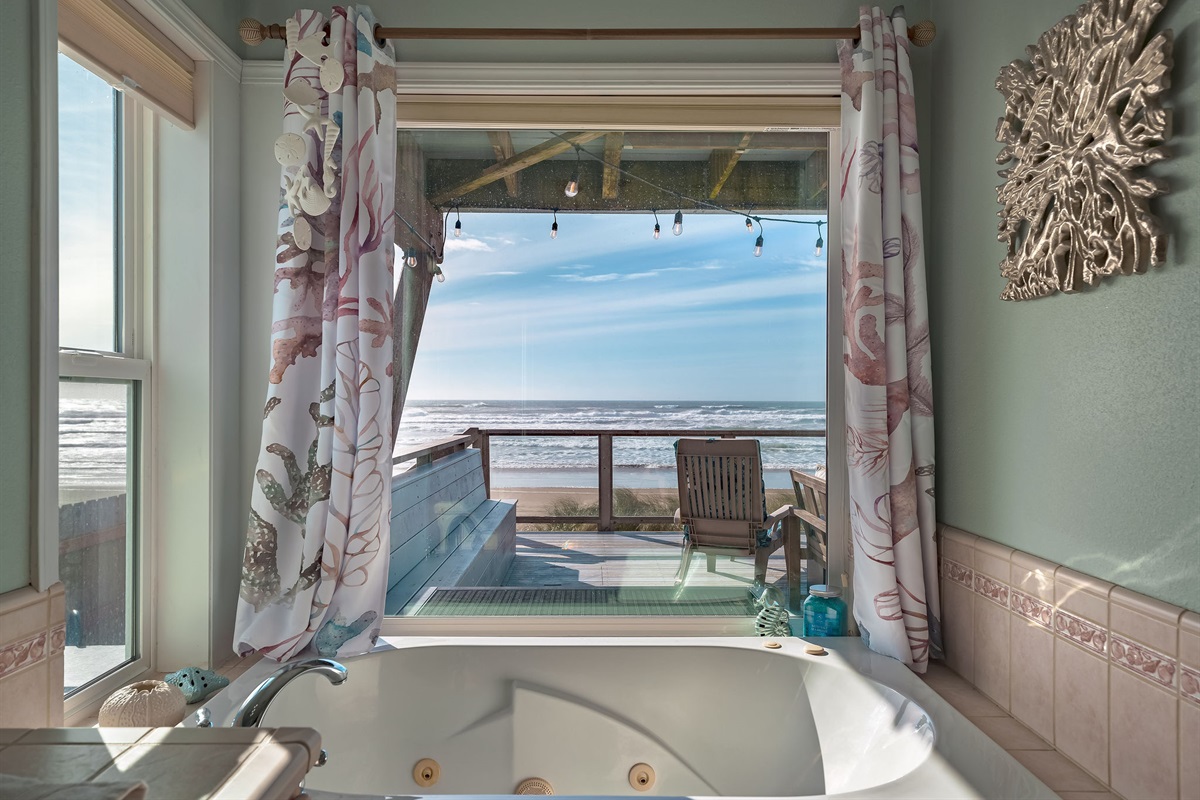 A big windowed bathroom offering a view of a calming beach and the ocean with a corner jacuzzi. 