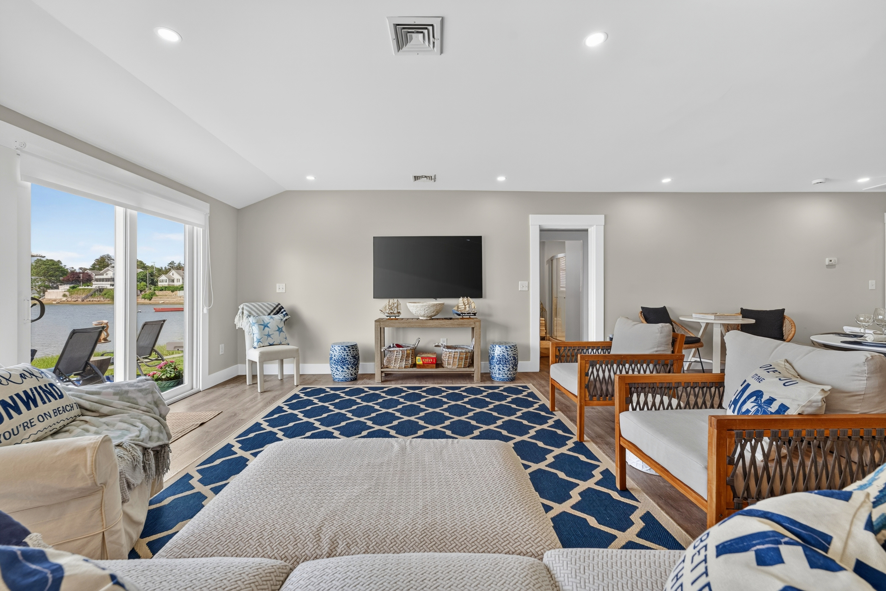 Bright open living room with fireplace, TV, dining area, and expansive windows facing the water.