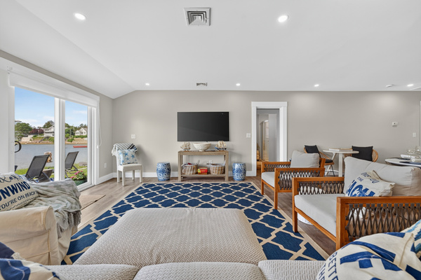 Bright open living room with fireplace, TV, dining area, and expansive windows facing the water.