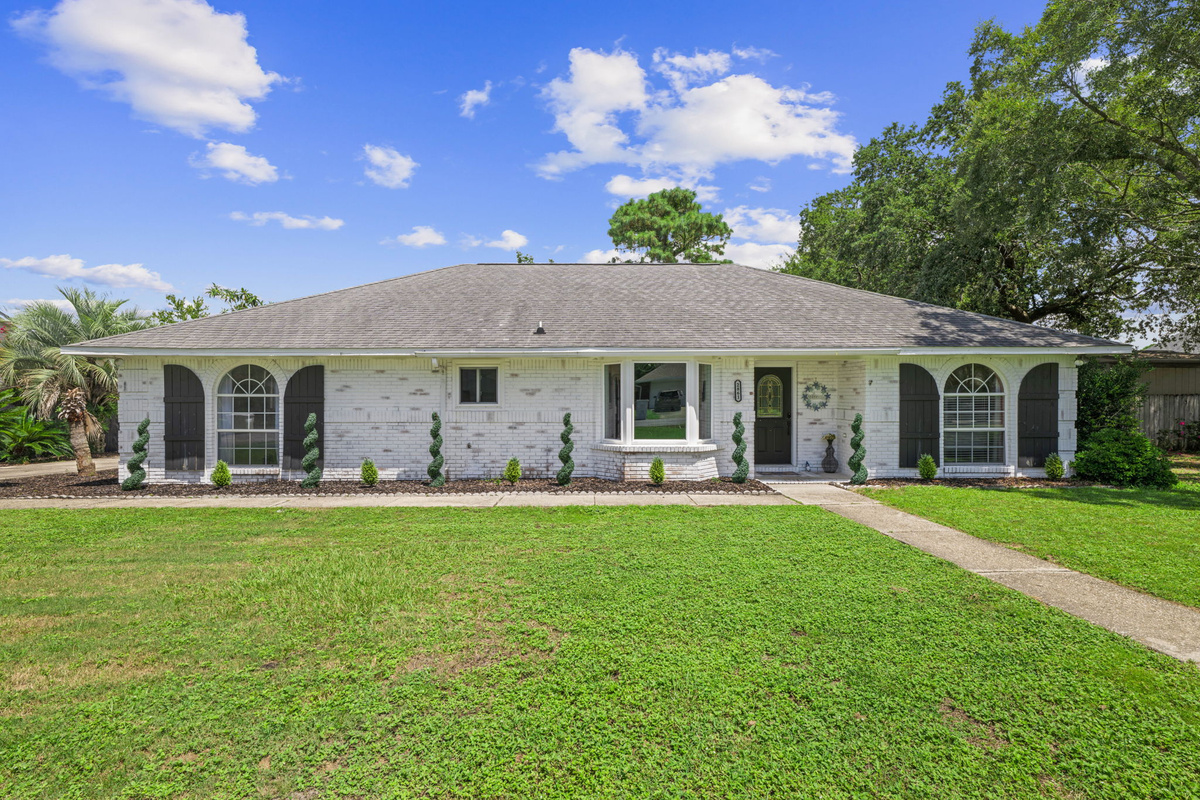 Your beach getaway starts here — a sunny, white-brick ranch with a manicured lawn and spiral topiaries lining the walkway.