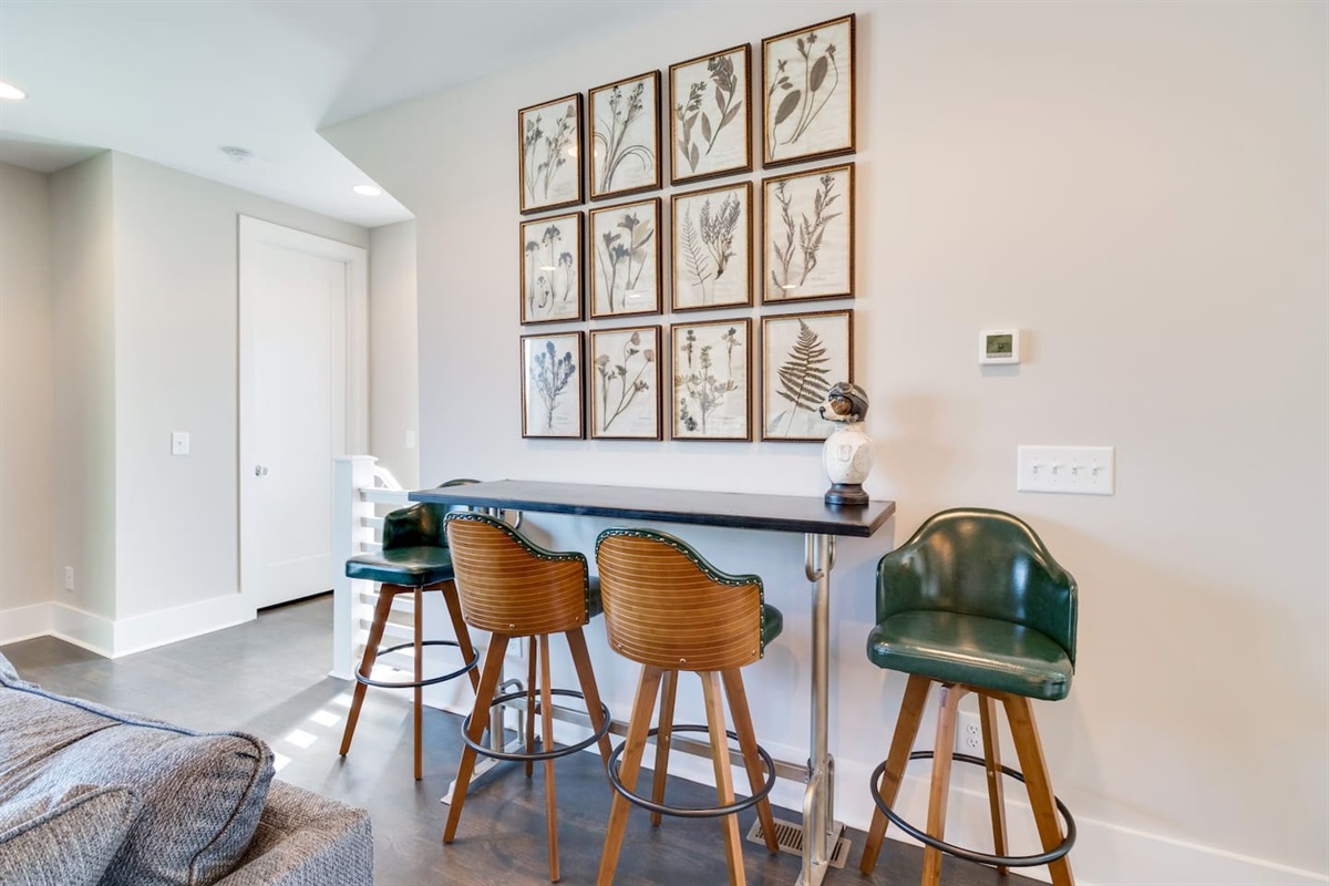 - Unique high top bar setup with four stylish stools perfect for morning coffee or cocktails - Wall art featuring botanical prints adds character & natural touch to the space - Positioned beside the living area for easy, casual entertaining or conversation