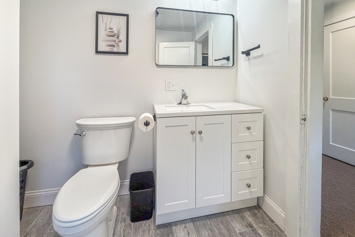 This wide interior shot highlights our upper level bathroom floor plan and white vanity cabinet layout. Featuring functional storage drawers, modern lighting, and a clear view to the hallway, this setup optimizes convenience for your Maine stay.