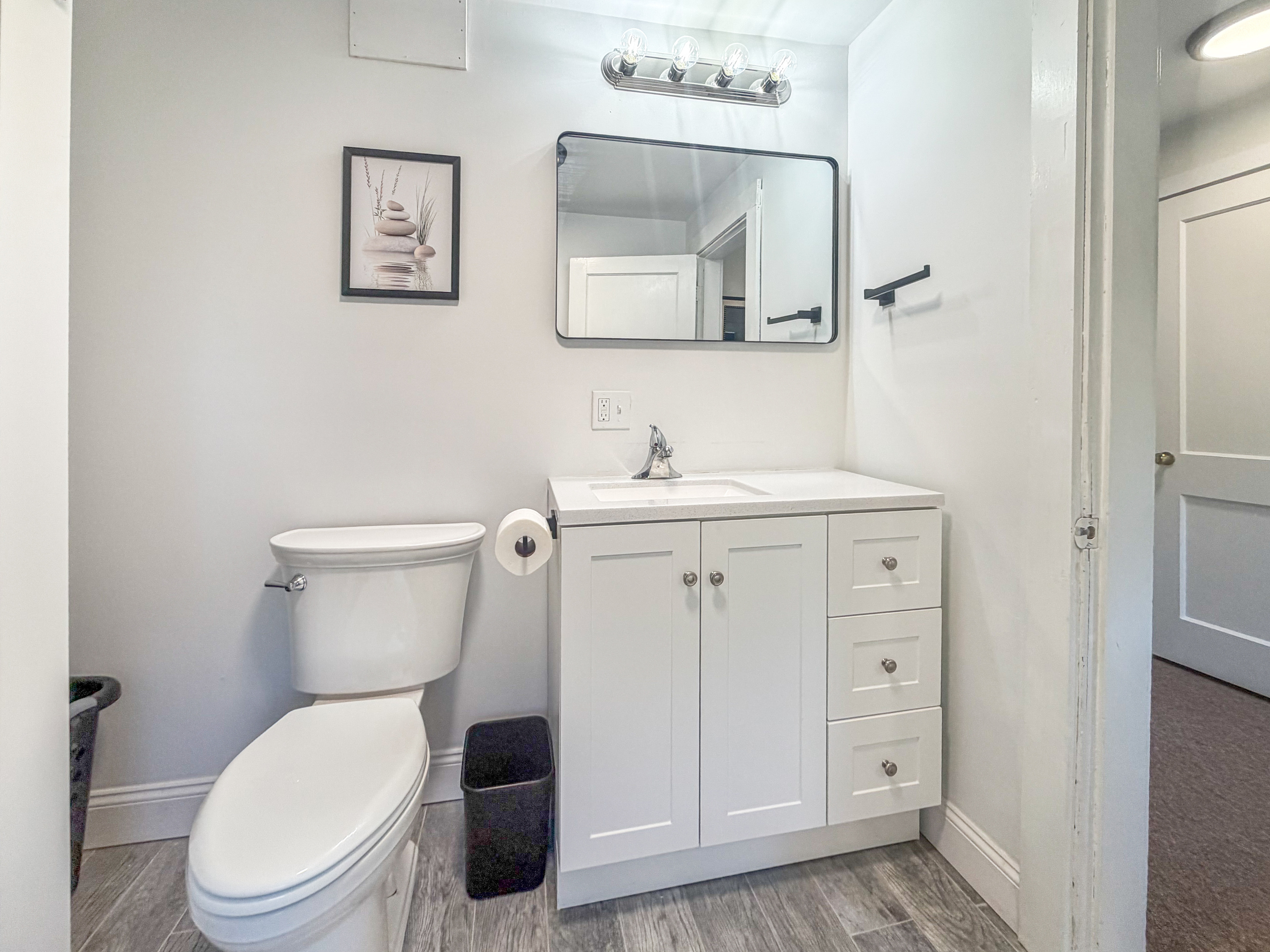 This wide interior shot highlights our upper level bathroom floor plan and white vanity cabinet layout. Featuring functional storage drawers, modern lighting, and a clear view to the hallway, this setup optimizes convenience for your Maine stay.
