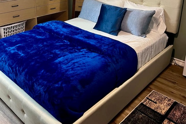 Queen bed with soft blue bedding and storage nearby for an easy stay.

