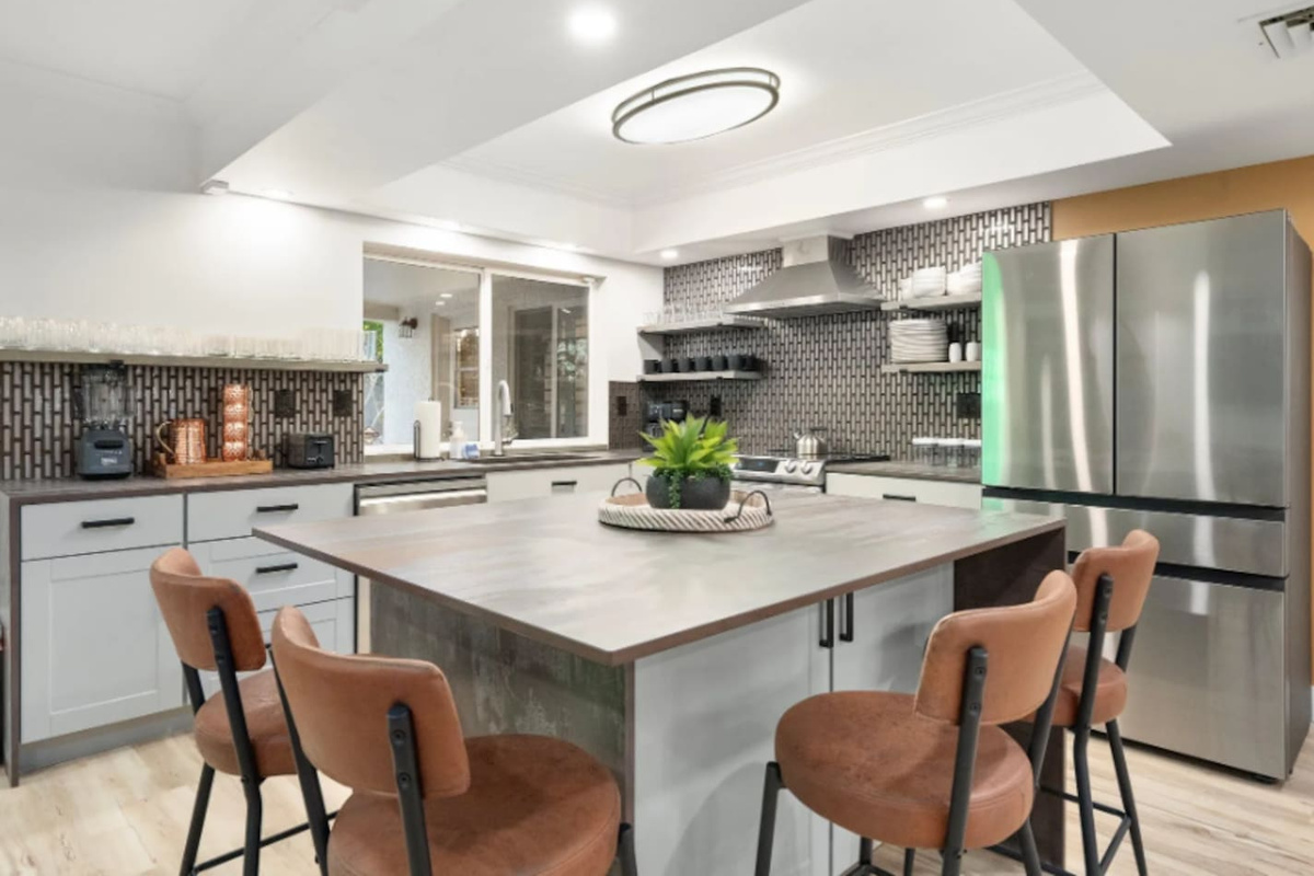 A spacious island with leather stools invites everyone to gather while the cook works their magic, with sleek stainless appliances rounding out the space.
