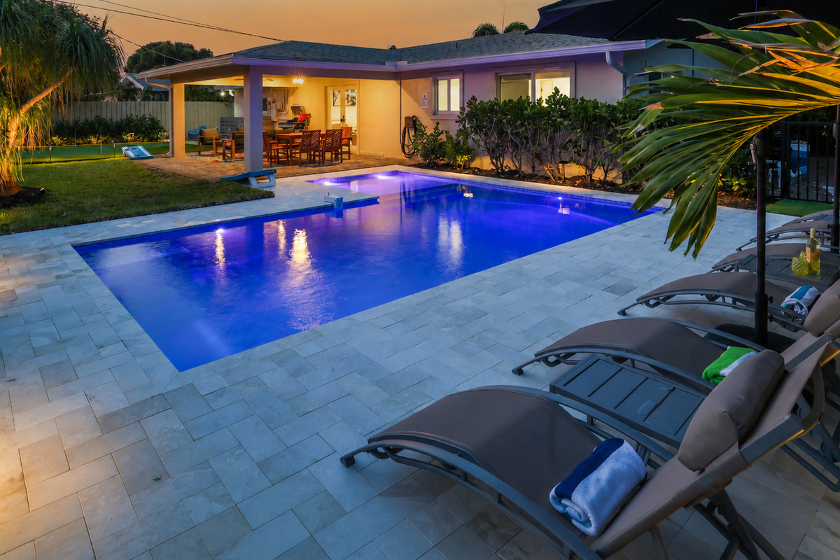 Twilight settles over the pool, patio, loungers, and palms, setting the tone for a relaxed Coastal Palms getaway.